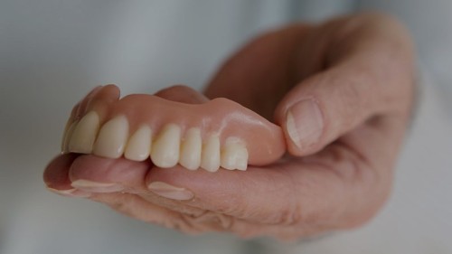 closeup of older womans hand holding a teeth denture